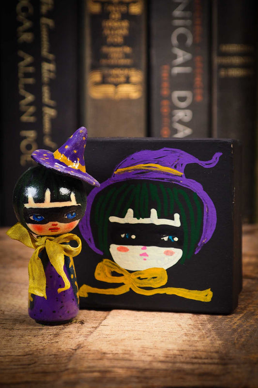 Small mini kokeshi Halloween art doll with black hair, purple witch hat, and yellow scarf, made by Idania Salcido, the artist behind Danita Art.