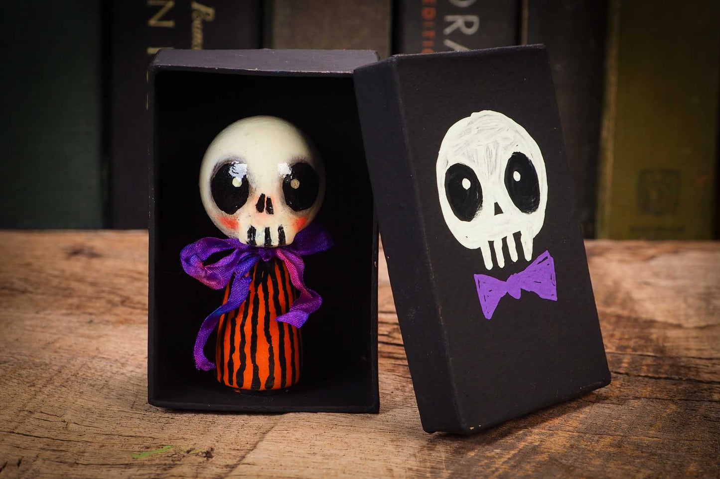 Small Halloween mini kokeshi art doll figurine with skull face, orange and black striped body, and purple ribbon. Made by Idania Salcido, Danita Art.