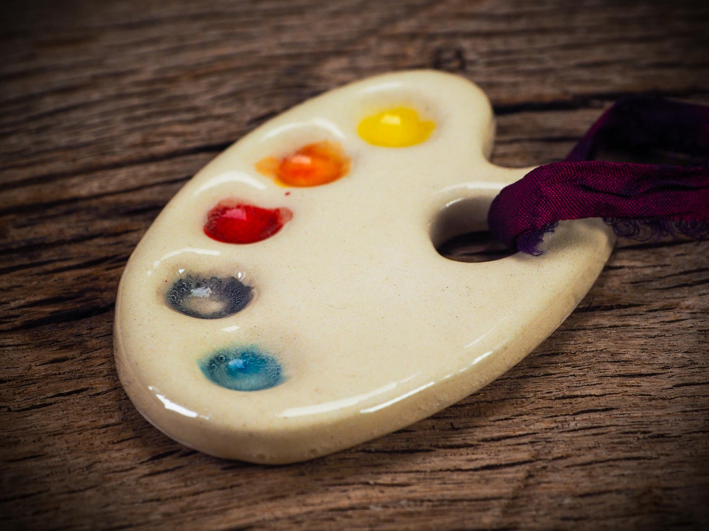 Handmade ceramic mini painter’s palette ornament with colorful paint wells, ideal as an artist gift or Christmas decoration by Idania Salcido - Danita Art.