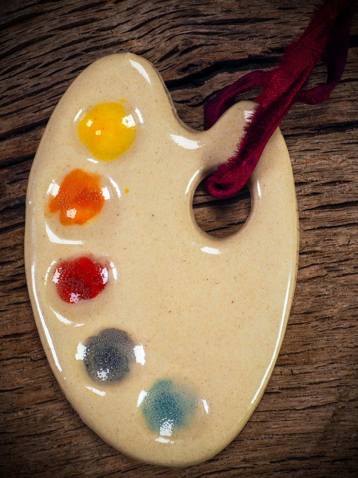 Handmade ceramic mini painter’s palette ornament with colorful paint wells, ideal as an artist gift or Christmas decoration by Idania Salcido Danita Art.