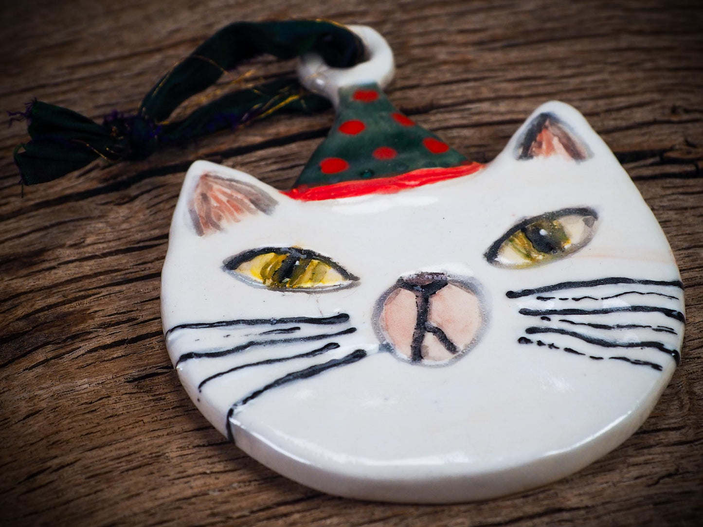 Handmade ceramic cat ornament with hand-painted face and festive hat, created by Idania Salcido - Danita Art for holiday decoration or gift giving.