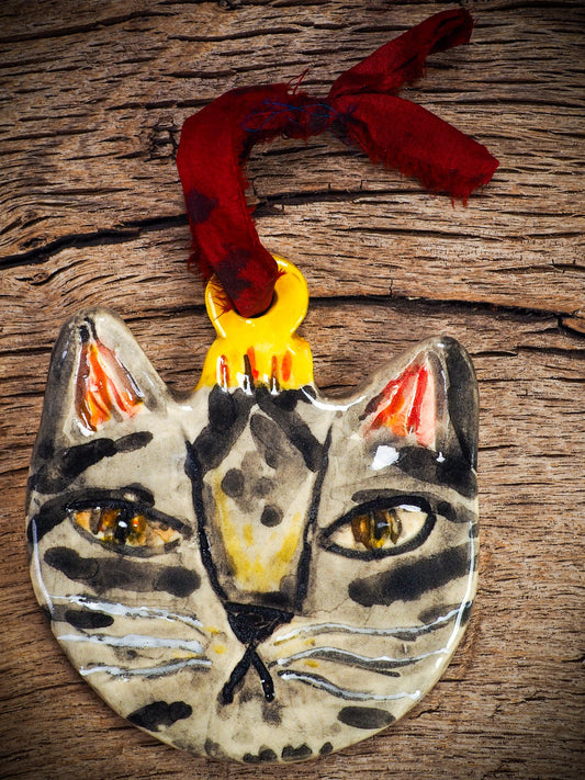 Handmade ceramic tabby cat ornament with painted stripes and ribbon, created by Idania Salcido Danita Art for holiday decorating or gifting.
