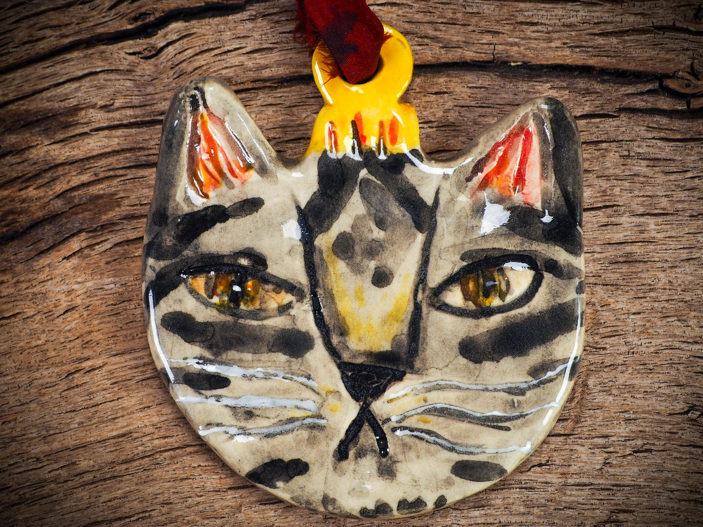 Handmade ceramic tabby cat ornament with painted stripes and ribbon, created by Idania Salcido Danita Art for holiday decorating or gifting.