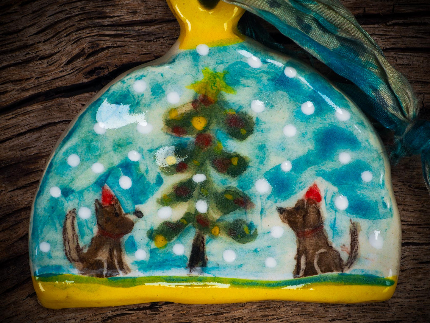 Handmade ceramic winter dogs ornament with snowy scene and ribbon, created by Idania Salcido Danita Art for Christmas decorating or gifting.