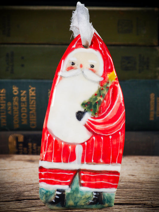 Handmade ceramic Santa figure ornament with red coat and ribbon, created by Danita Art for Christmas decoration or gifting.