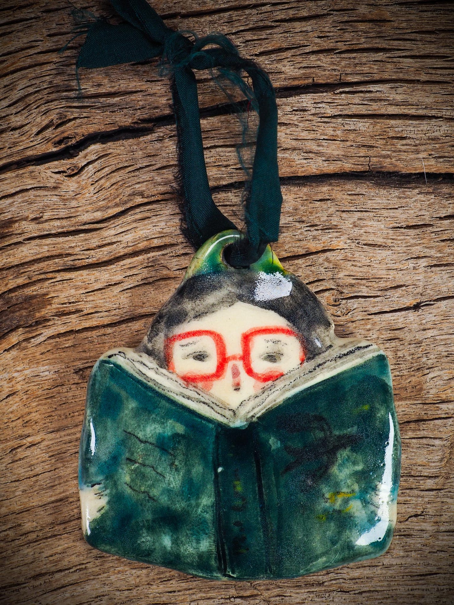 Handmade ceramic reader ornament with red glasses and green book, created by Idania Salcido aka Danita Art for Christmas decorating or gifting.