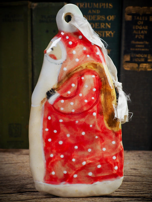Handmade ceramic winter figure ornament with red dotted coat and ribbon, created by Idania Salcido AKA Danita Art for Christmas decorating or gifting.