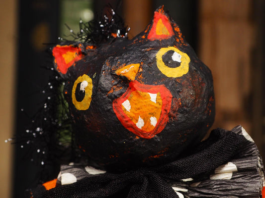 A close-up of a handmade black cat Halloween decoration with orange and yellow painted details, black tinsel hair, and a black-and-white polka-dotted scarf.
An original handmade spun cotton Halloween art doll by Idania Salcido (Danita Art).