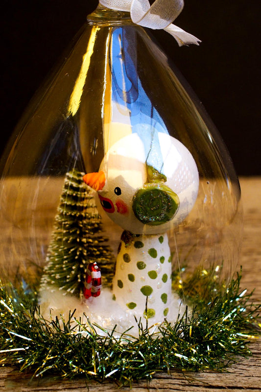 An original handmade christmas tree ornament by Idania Salcido. A clear domed diorama with a holiday scene with Santa Claus elves, Christmas Trees, Elves, Gifts and magical glitter deer.