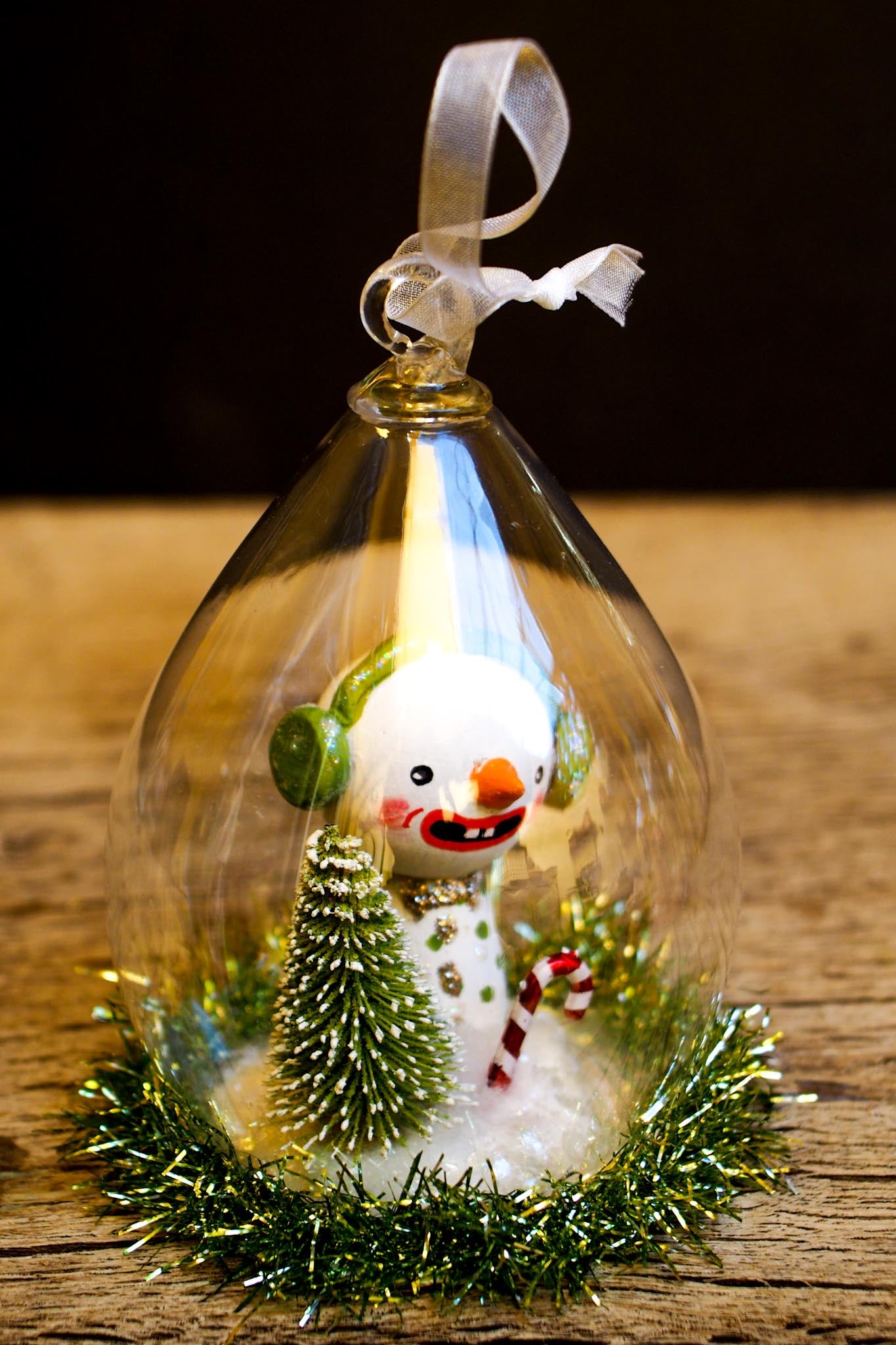 An original handmade christmas tree ornament by Idania Salcido. A clear domed diorama with a holiday scene with Santa Claus elves, Christmas Trees, Elves, Gifts and magical glitter deer.