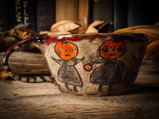 Fire glazed ceramic coffee mug by Idania Salcido, Danita Art. On Halloween, Danita creates ceramic containers for pumpkin spice coffee, warm tea or sweets to give on trick-or-treat night. With carved with Halloween ghosts, skeletons, witches, ghouls, black cats, jack-o-lanterns, item is food safe, hand wash only.