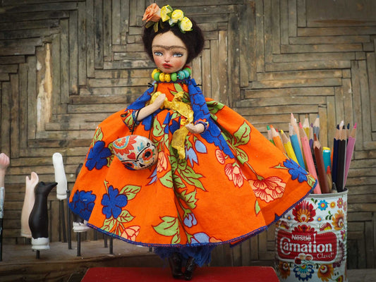A beautiful handmade art doll by Danita, inspired by Mexican Folk art, Frida Kahlo and The Day Of the Dead. She wears a colorful native motif dress, an unmistakable unibrow, a colorful Dia De los Muertos Catrina skull mask and the signature amazing eyes of Danita Art.