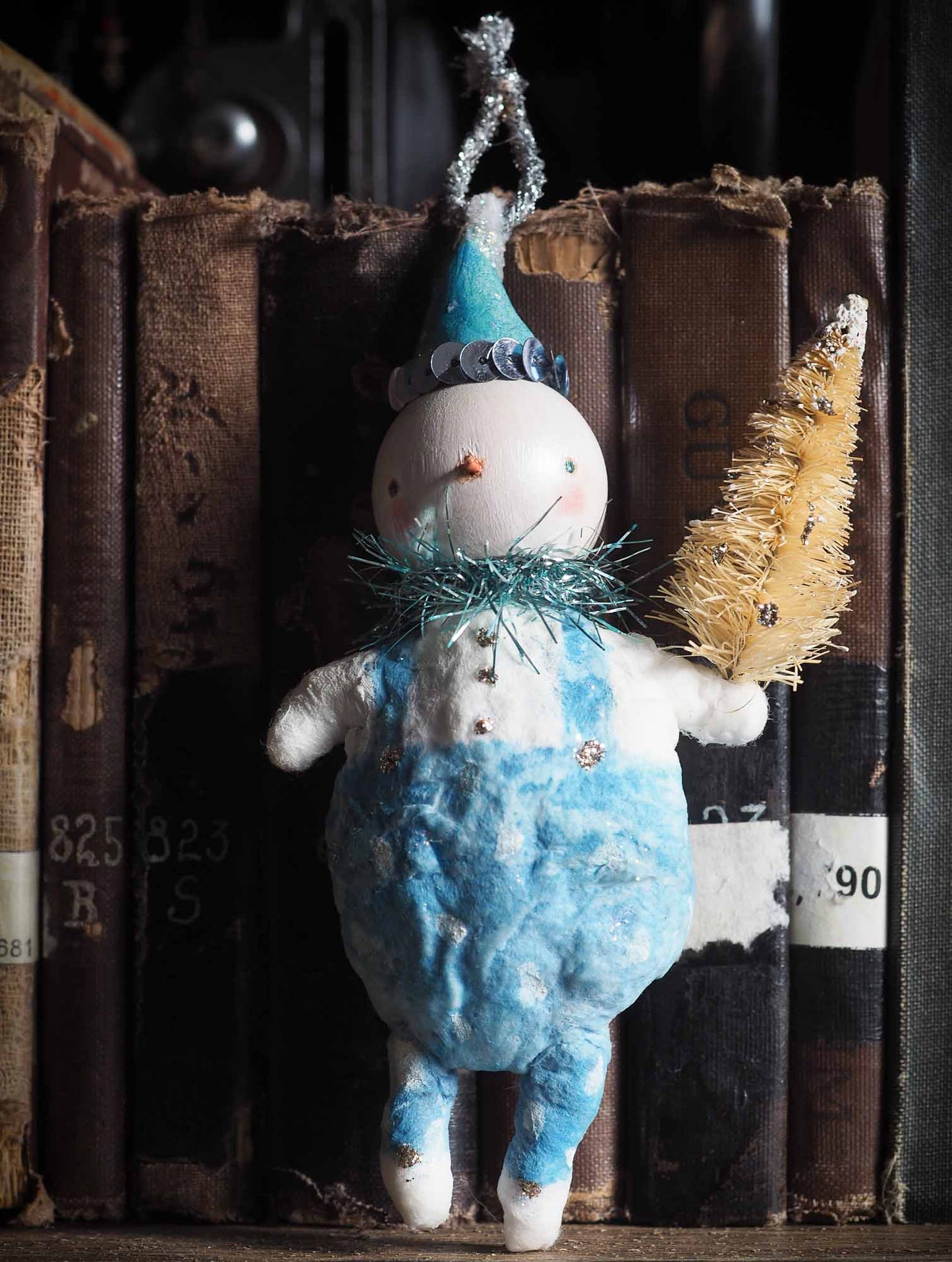 Spun cotton hand made ornament snowman by Danita Art. Made with organic cotton, painted in a vintage, folk art weathered style resembling Christmas tree handmade decorations from 19th century. Has bristle bottle brush tree, and decorative accents with glitter. Ready to hang on vintage tinsel ribbon on Christmas tree.