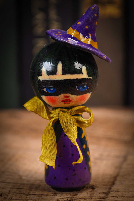 Small mini kokeshi Halloween art doll with black hair, purple witch hat, and yellow scarf, made by Idania Salcido, the artist behind Danita Art.