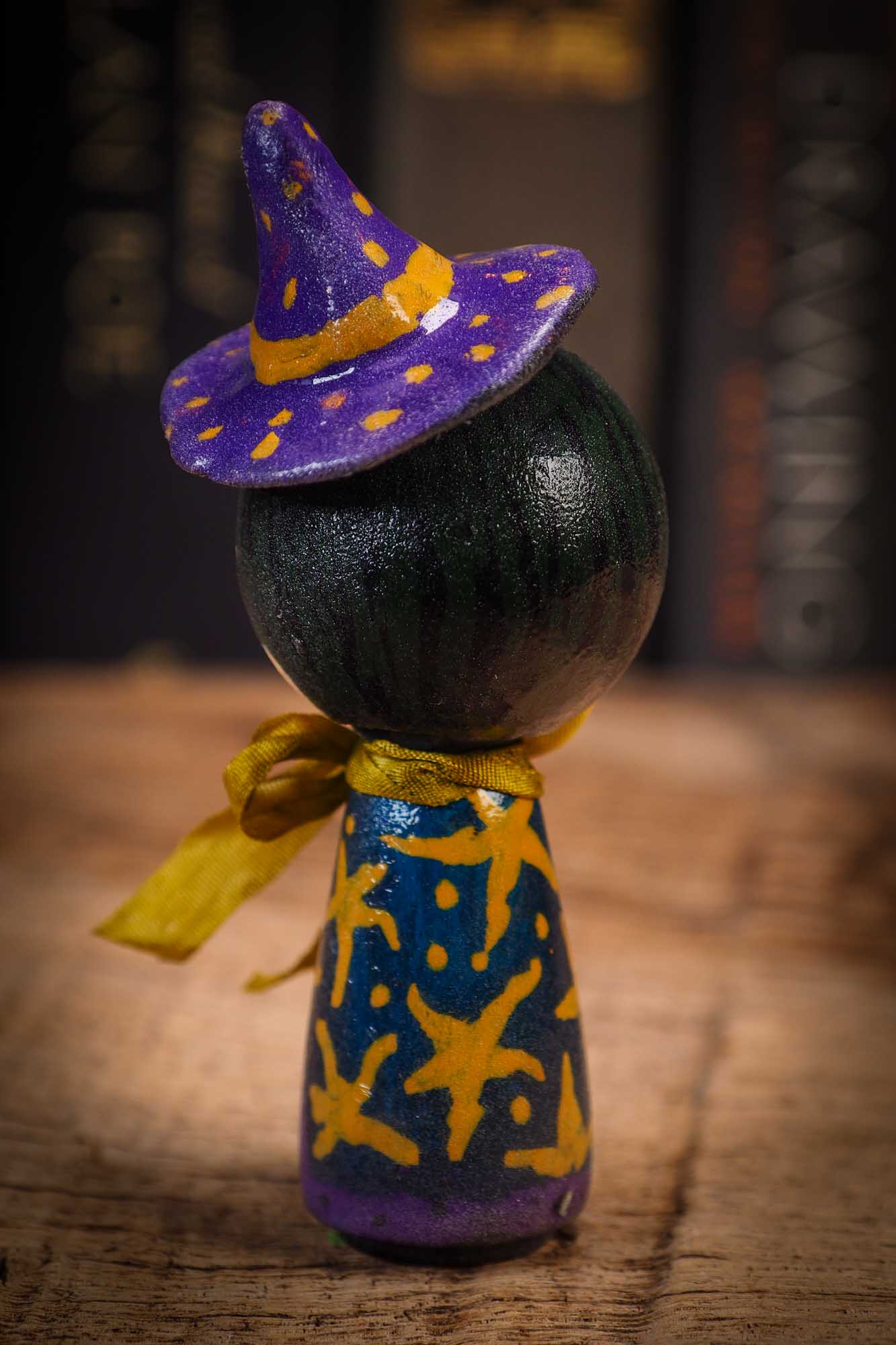 Small mini kokeshi Halloween art doll with black hair, purple witch hat, and yellow scarf, made by Idania Salcido, the artist behind Danita Art.