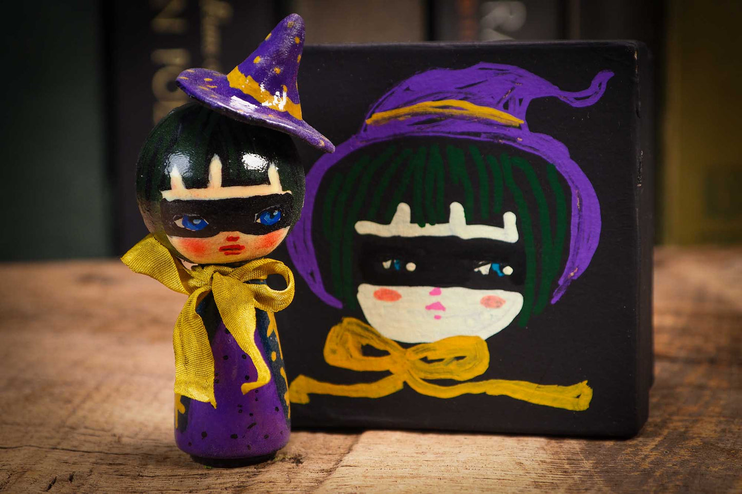 Small mini kokeshi Halloween art doll with black hair, purple witch hat, and yellow scarf, made by Idania Salcido, the artist behind Danita Art.