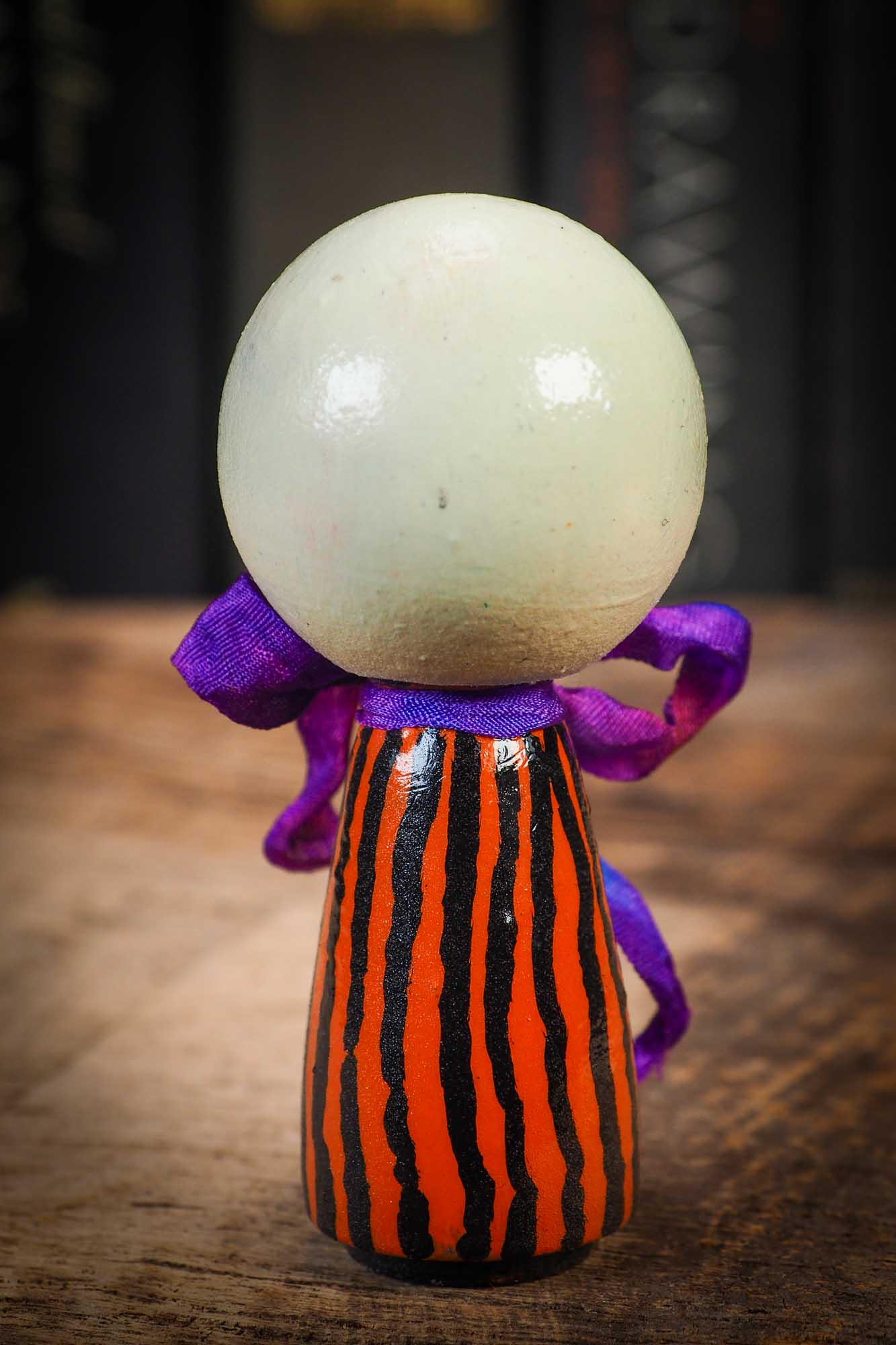 Small Halloween mini kokeshi art doll figurine with skull face, orange and black striped body, and purple ribbon. Made by Idania Salcido, Danita Art.