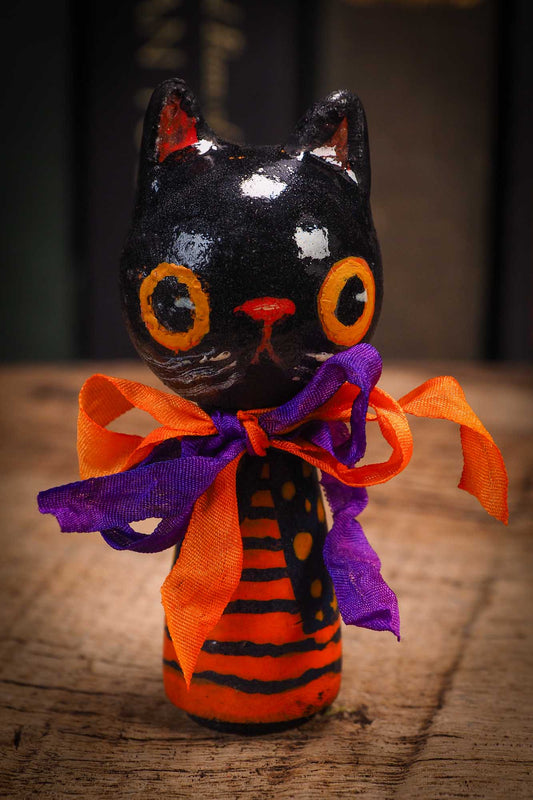 Small Halloween mini kokeshi art doll figurine with black cat face, orange and black striped body, purple and orange ribbon. Made by Idania Salcido, Danita Art.