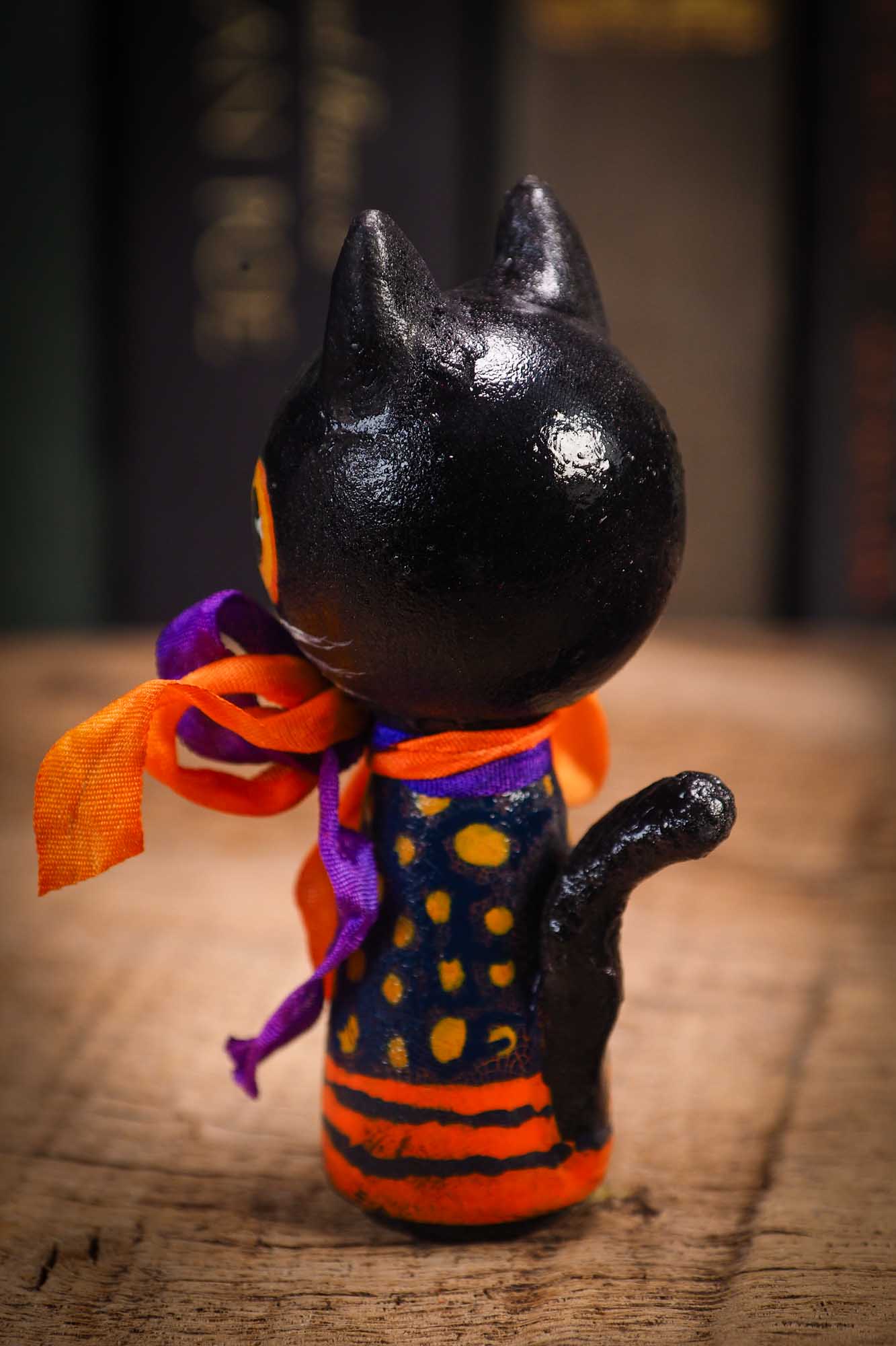 Small Halloween mini kokeshi art doll figurine with black cat face, orange and black striped body, purple and orange ribbon. Made by Idania Salcido, Danita Art.