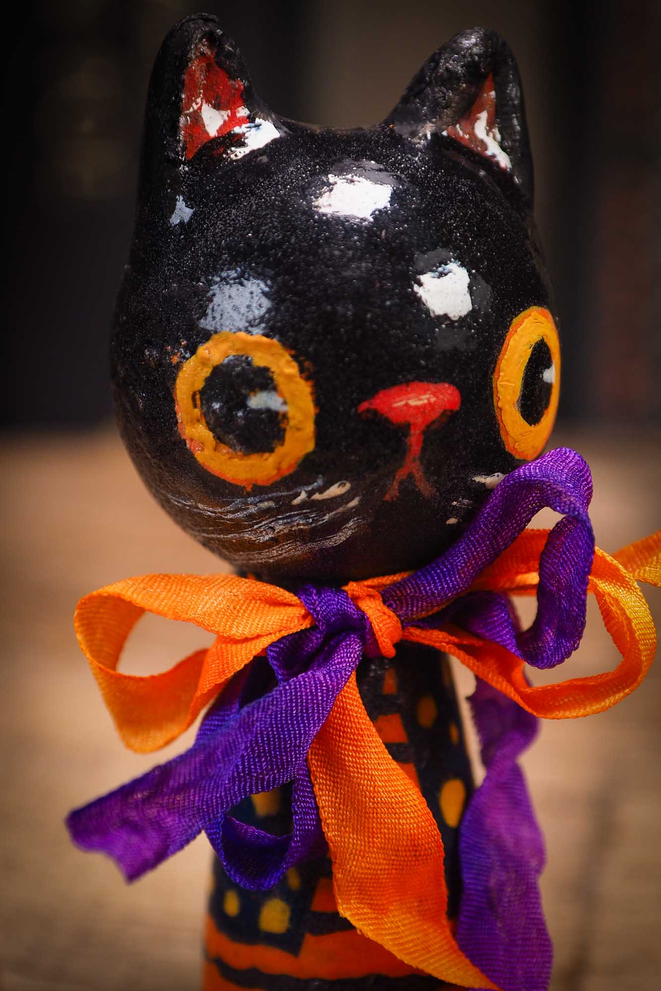 Small Halloween mini kokeshi art doll figurine with black cat face, orange and black striped body, purple and orange ribbon. Made by Idania Salcido, Danita Art.