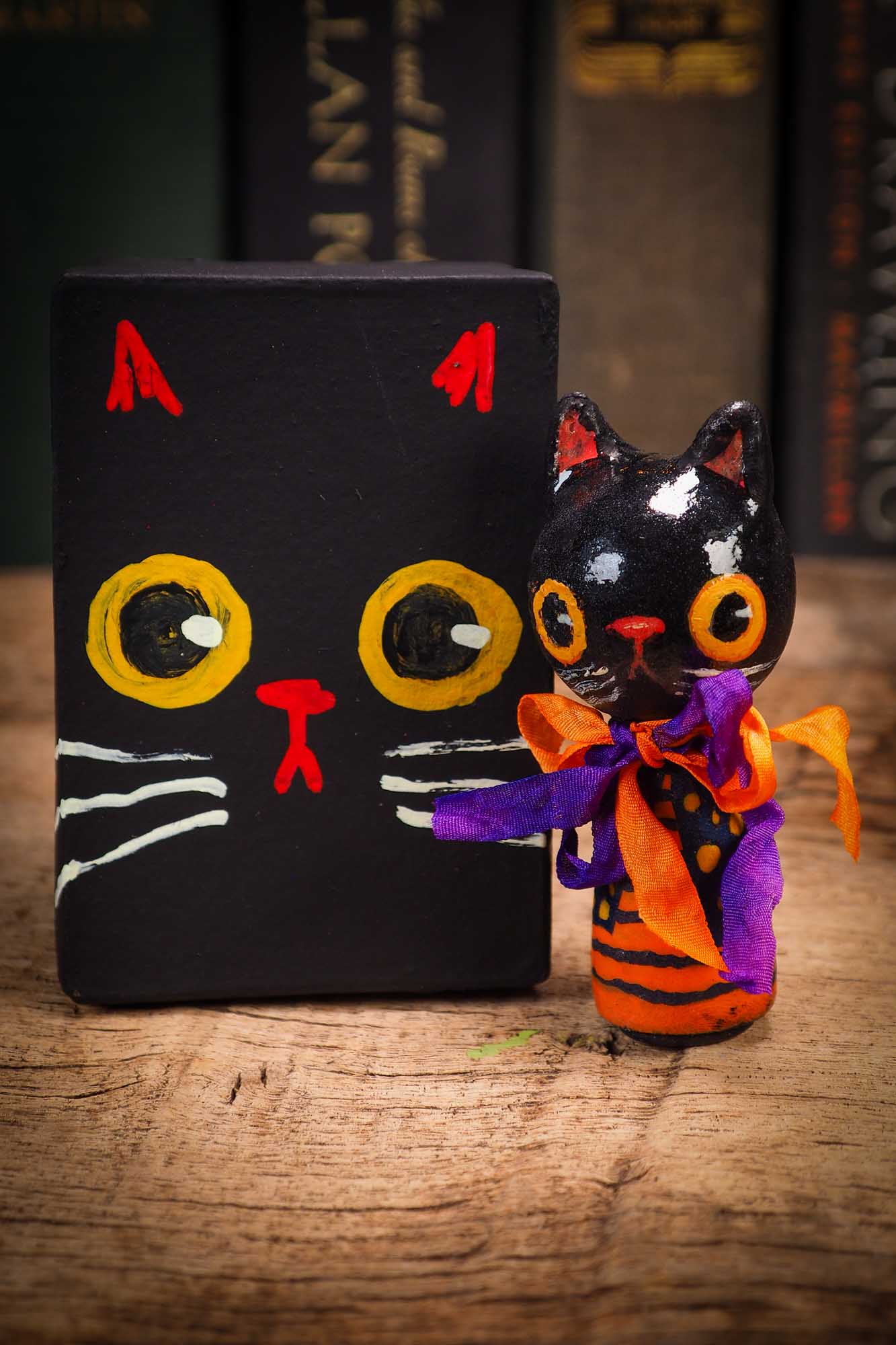 Small Halloween mini kokeshi art doll figurine with black cat face, orange and black striped body, purple and orange ribbon. Made by Idania Salcido, Danita Art.