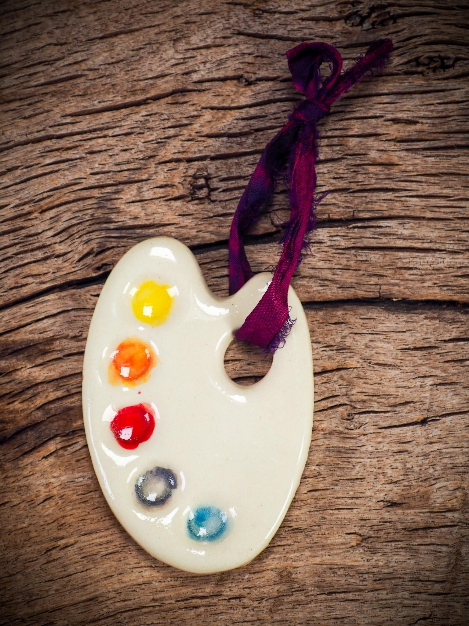 Handmade ceramic mini painter’s palette ornament with colorful paint wells, ideal as an artist gift or Christmas decoration by Idania Salcido - Danita Art.