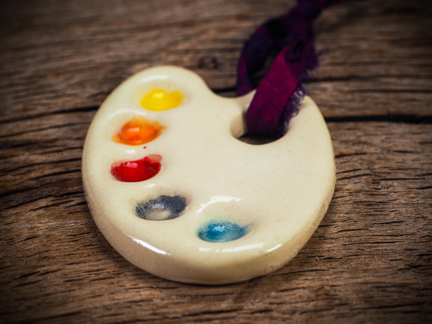 Handmade ceramic mini painter’s palette ornament with colorful paint wells, ideal as an artist gift or Christmas decoration by Idania Salcido - Danita Art.