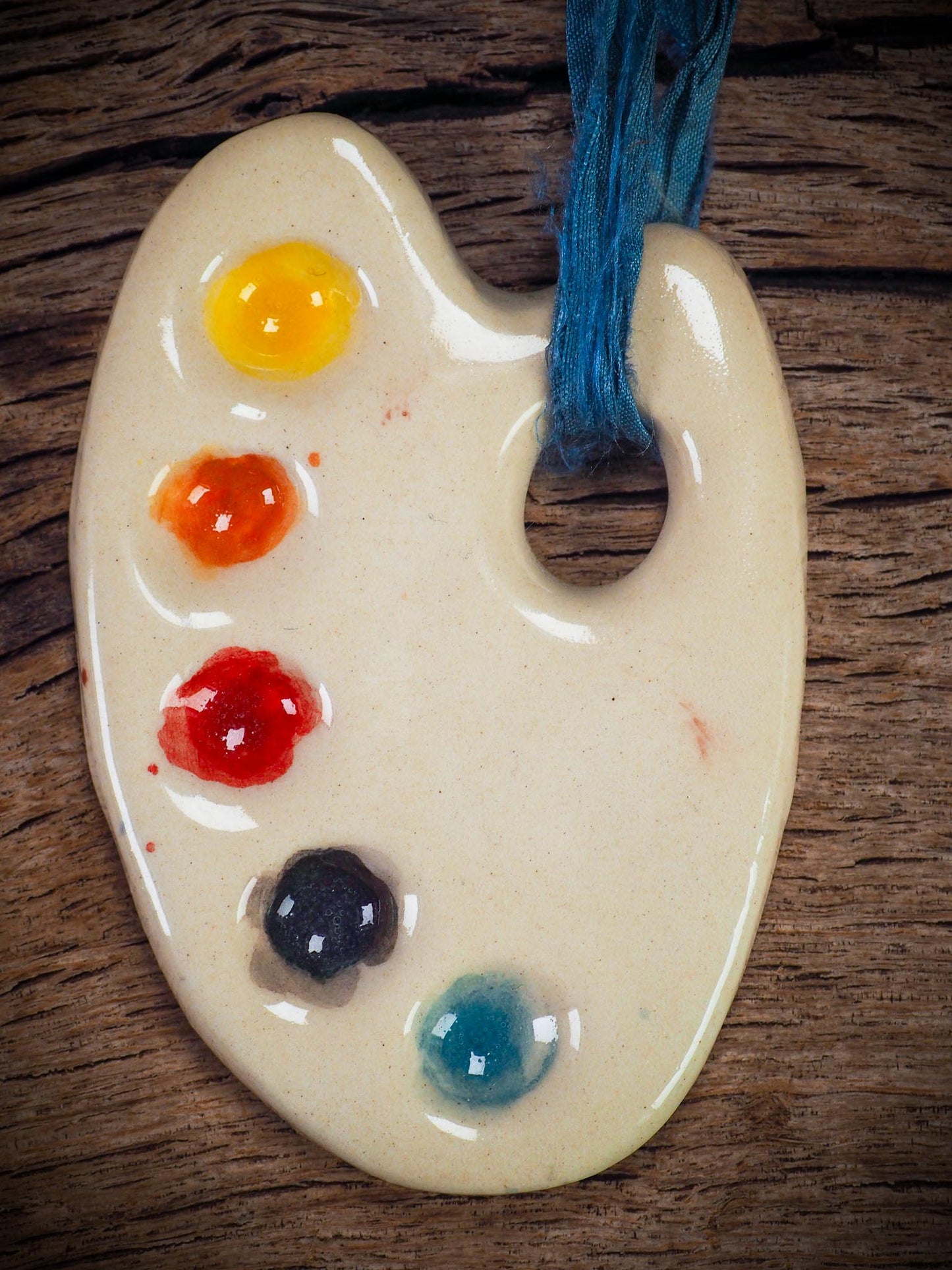 Handmade ceramic mini painter’s palette ornament with colorful paint wells, ideal as an artist gift or Christmas decoration by Idania Salcido Danita Art.