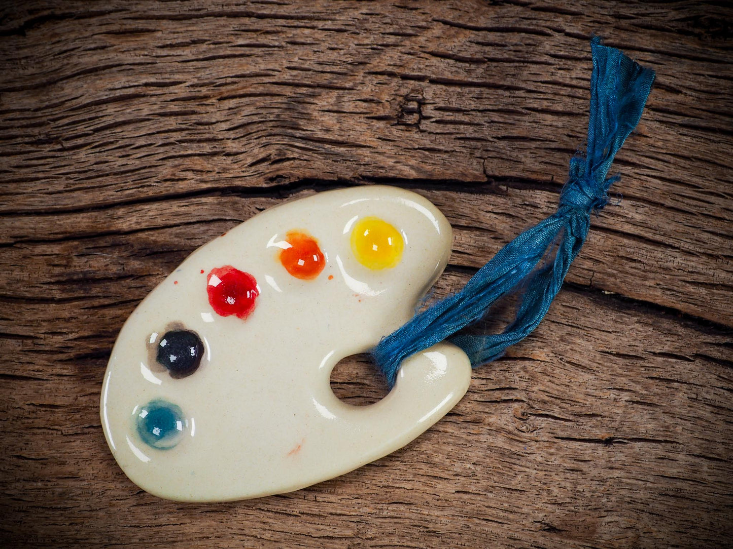 Handmade ceramic mini painter’s palette ornament with colorful paint wells, ideal as an artist gift or Christmas decoration by Idania Salcido Danita Art.