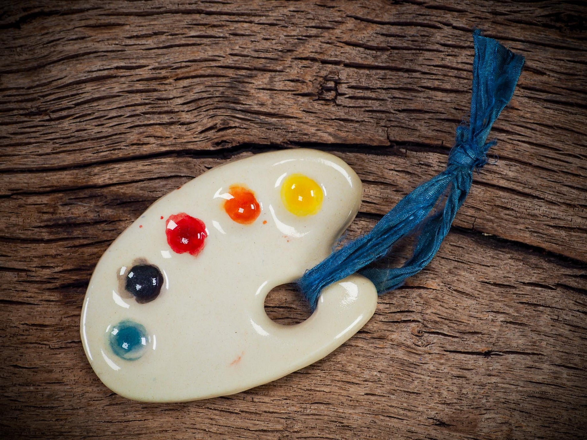 Handmade ceramic mini painter’s palette ornament with colorful paint wells, ideal as an artist gift or Christmas decoration by Idania Salcido Danita Art.