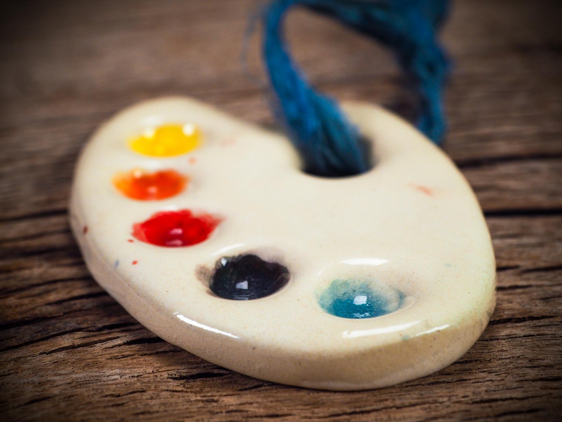 Handmade ceramic mini painter’s palette ornament with colorful paint wells, ideal as an artist gift or Christmas decoration by Idania Salcido Danita Art.