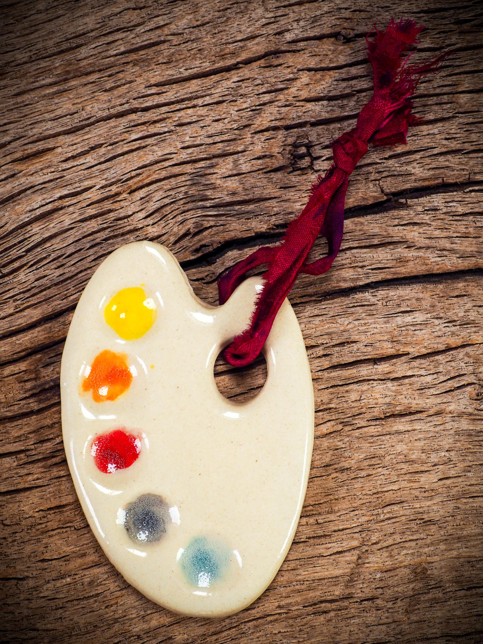 Handmade ceramic mini painter’s palette ornament with colorful paint wells, ideal as an artist gift or Christmas decoration by Idania Salcido Danita Art.
