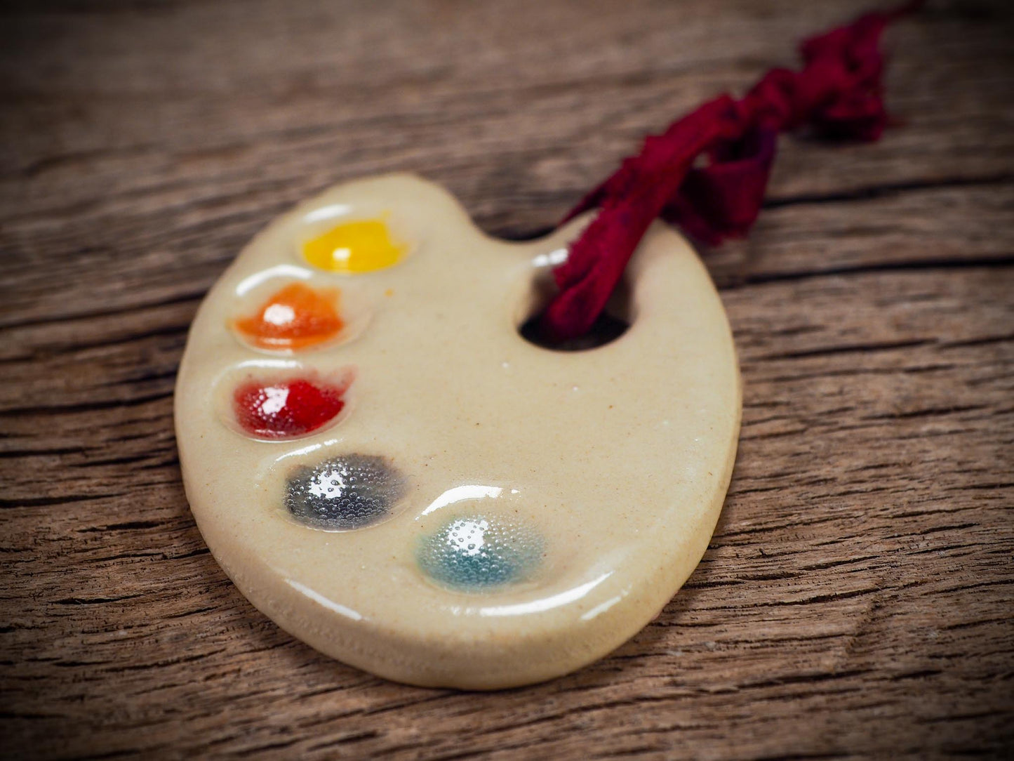 Handmade ceramic mini painter’s palette ornament with colorful paint wells, ideal as an artist gift or Christmas decoration by Idania Salcido Danita Art.