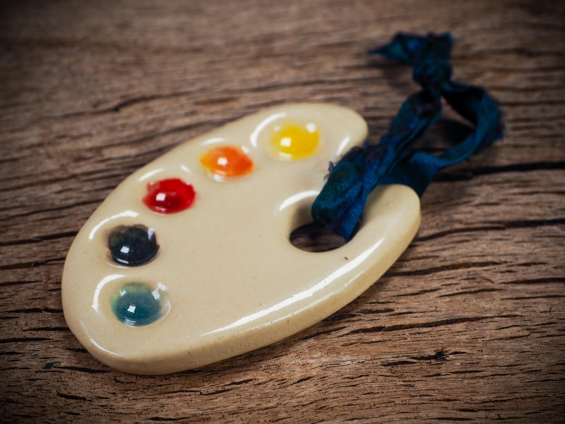 Handmade ceramic mini painter’s palette ornament with colorful paint wells, ideal as an artist gift or Christmas decoration by Idania Salcido Danita Art.