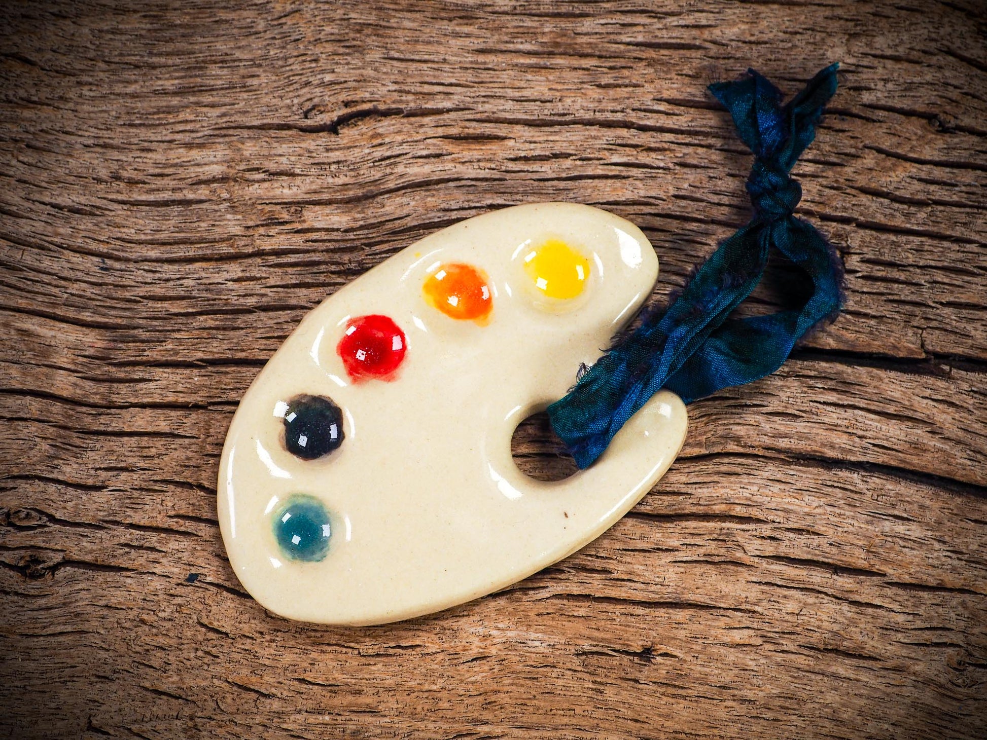 Handmade ceramic mini painter’s palette ornament with colorful paint wells, ideal as an artist gift or Christmas decoration by Idania Salcido Danita Art.