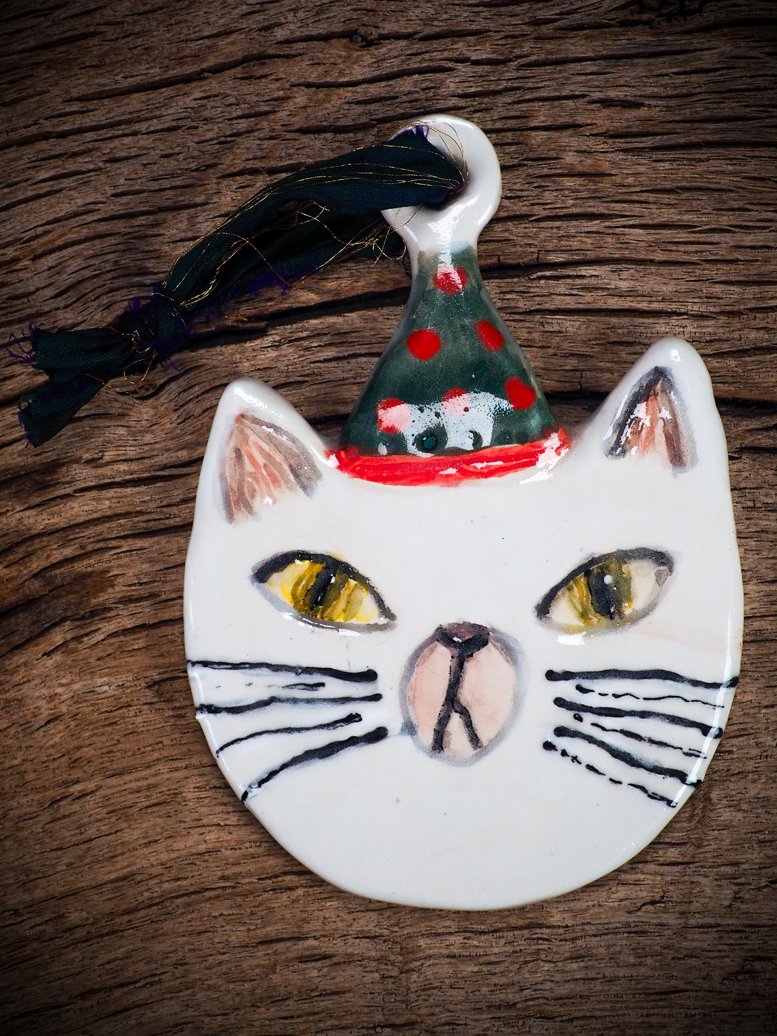 Handmade ceramic cat ornament with hand-painted face and festive hat, created by Idania Salcido - Danita Art for holiday decoration or gift giving.