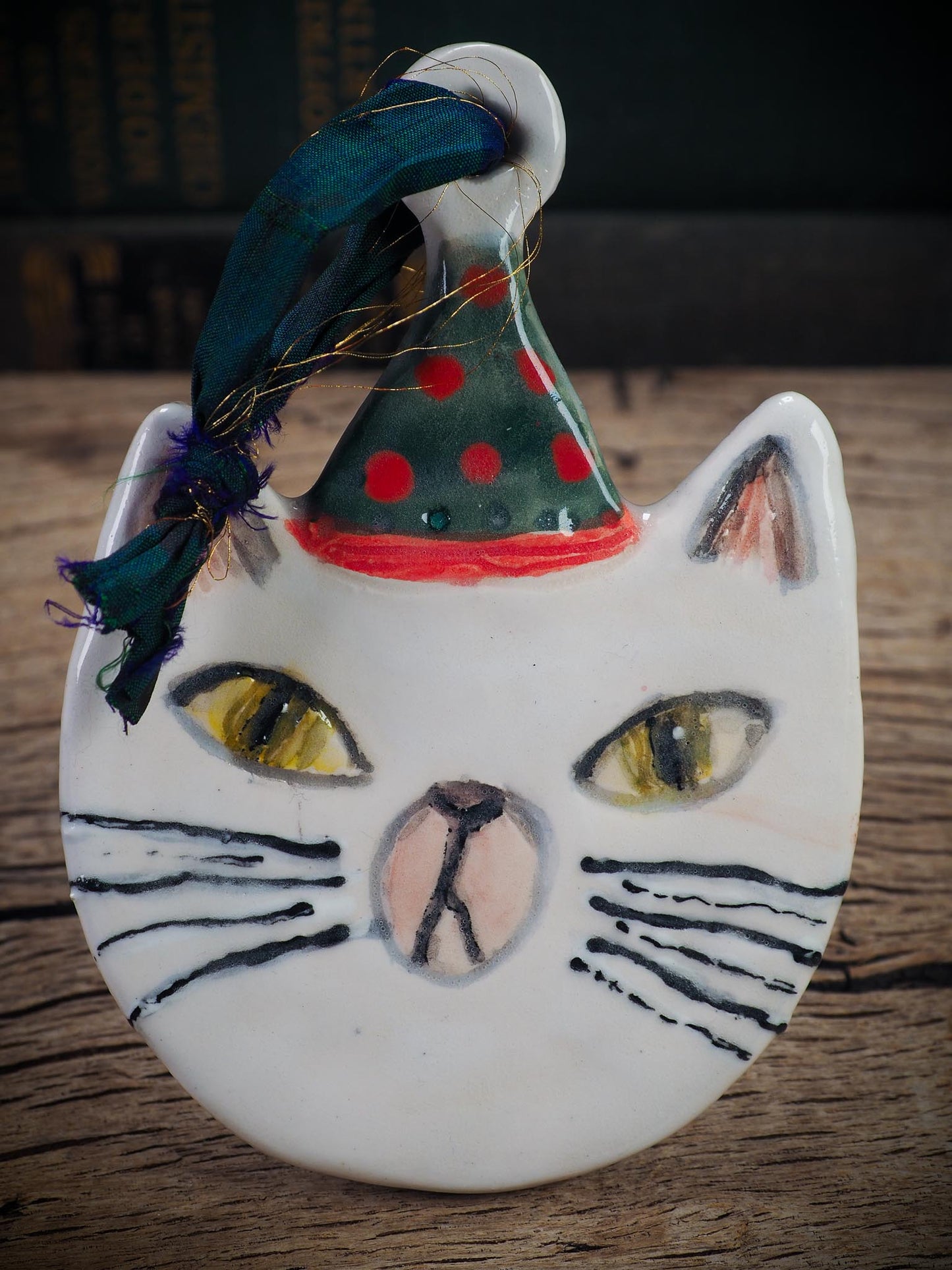 Handmade ceramic cat ornament with hand-painted face and festive hat, created by Idania Salcido - Danita Art for holiday decoration or gift giving.