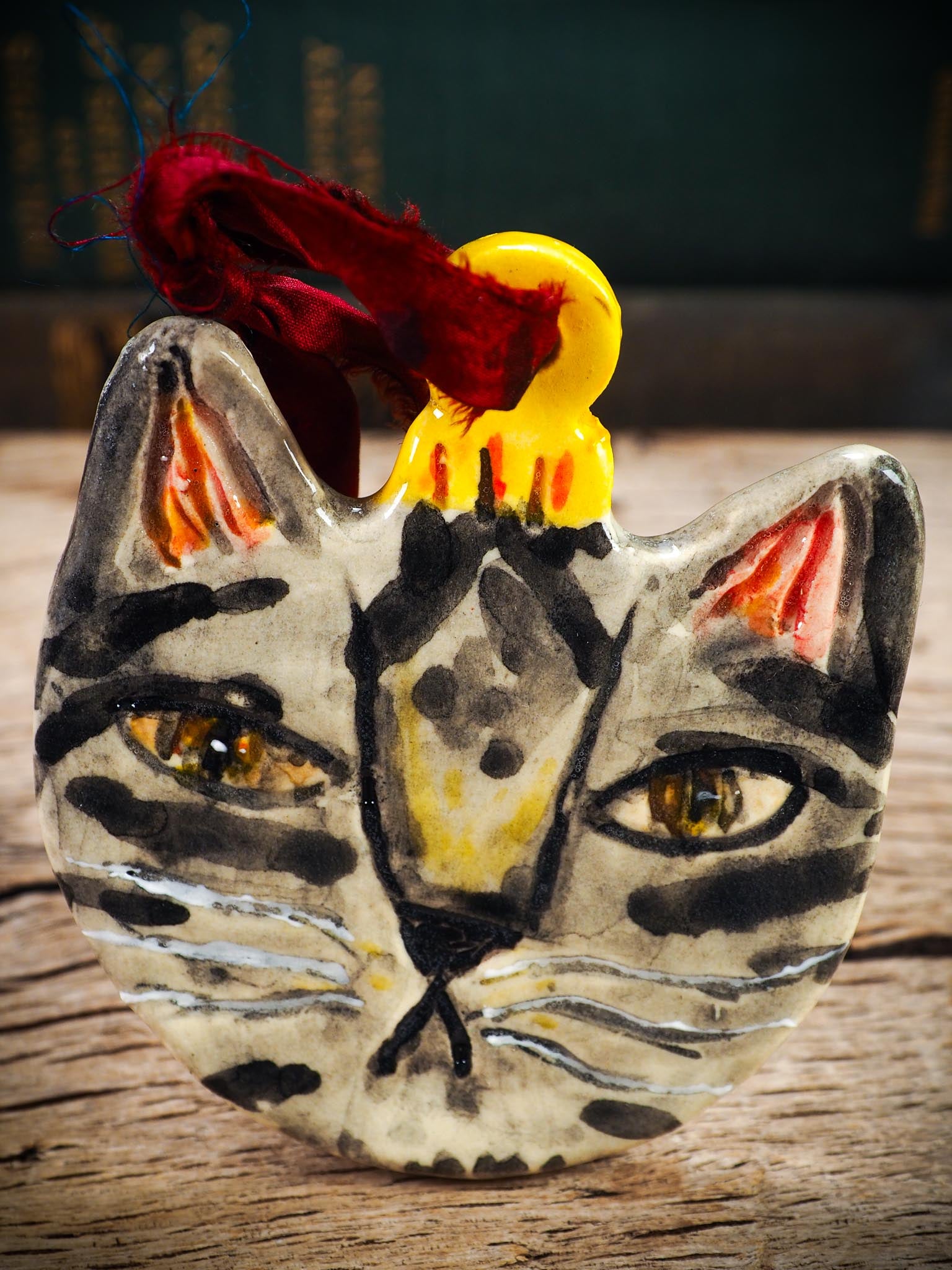 Handmade ceramic tabby cat ornament with painted stripes and ribbon, created by Idania Salcido Danita Art for holiday decorating or gifting.