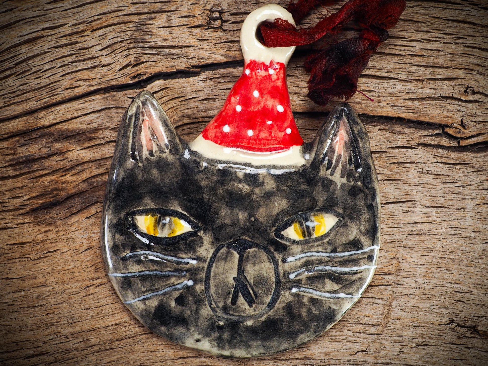 Handmade ceramic black cat ornament named Loki with red holiday hat and ribbon, created by Danita Art Idania Salcido for Christmas decorating or gifting.