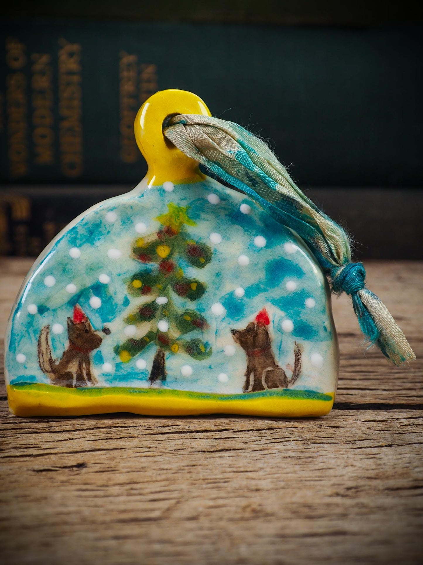 Handmade ceramic winter dogs ornament with snowy scene and ribbon, created by Idania Salcido Danita Art for Christmas decorating or gifting.