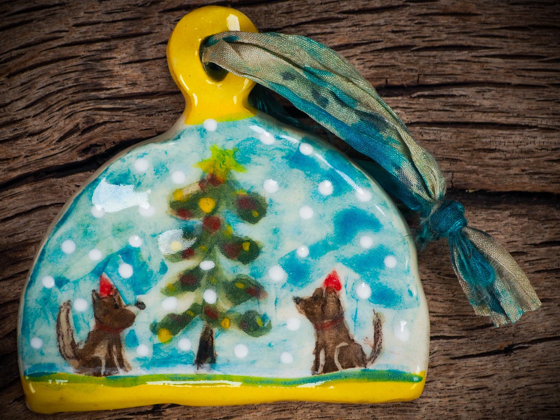 Handmade ceramic winter dogs ornament with snowy scene and ribbon, created by Idania Salcido Danita Art for Christmas decorating or gifting.