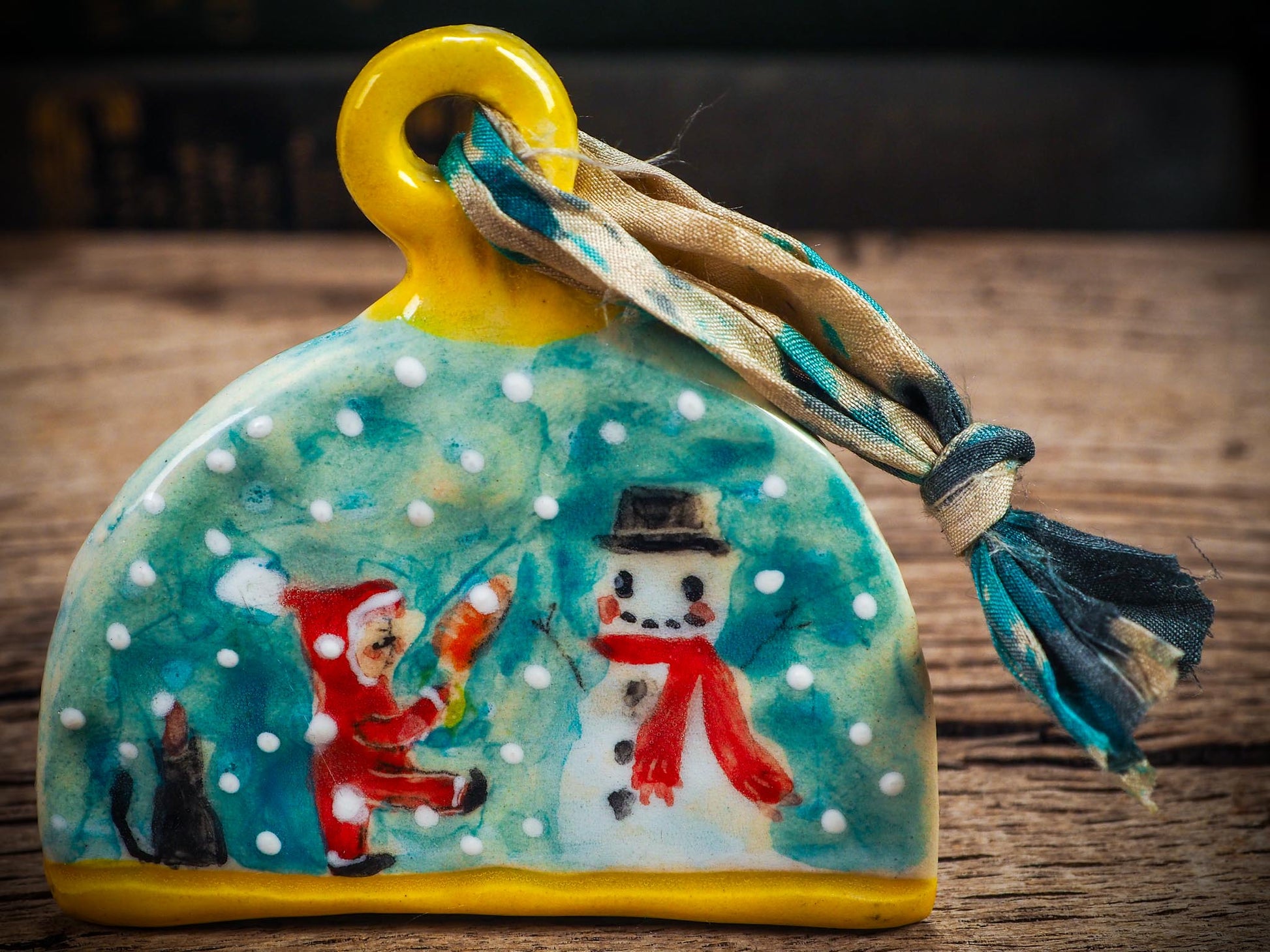 Handmade ceramic ornament with snowman, little Santa, and snowfall, created by Idania Salcido Danita Art for Christmas decorating or gifting.