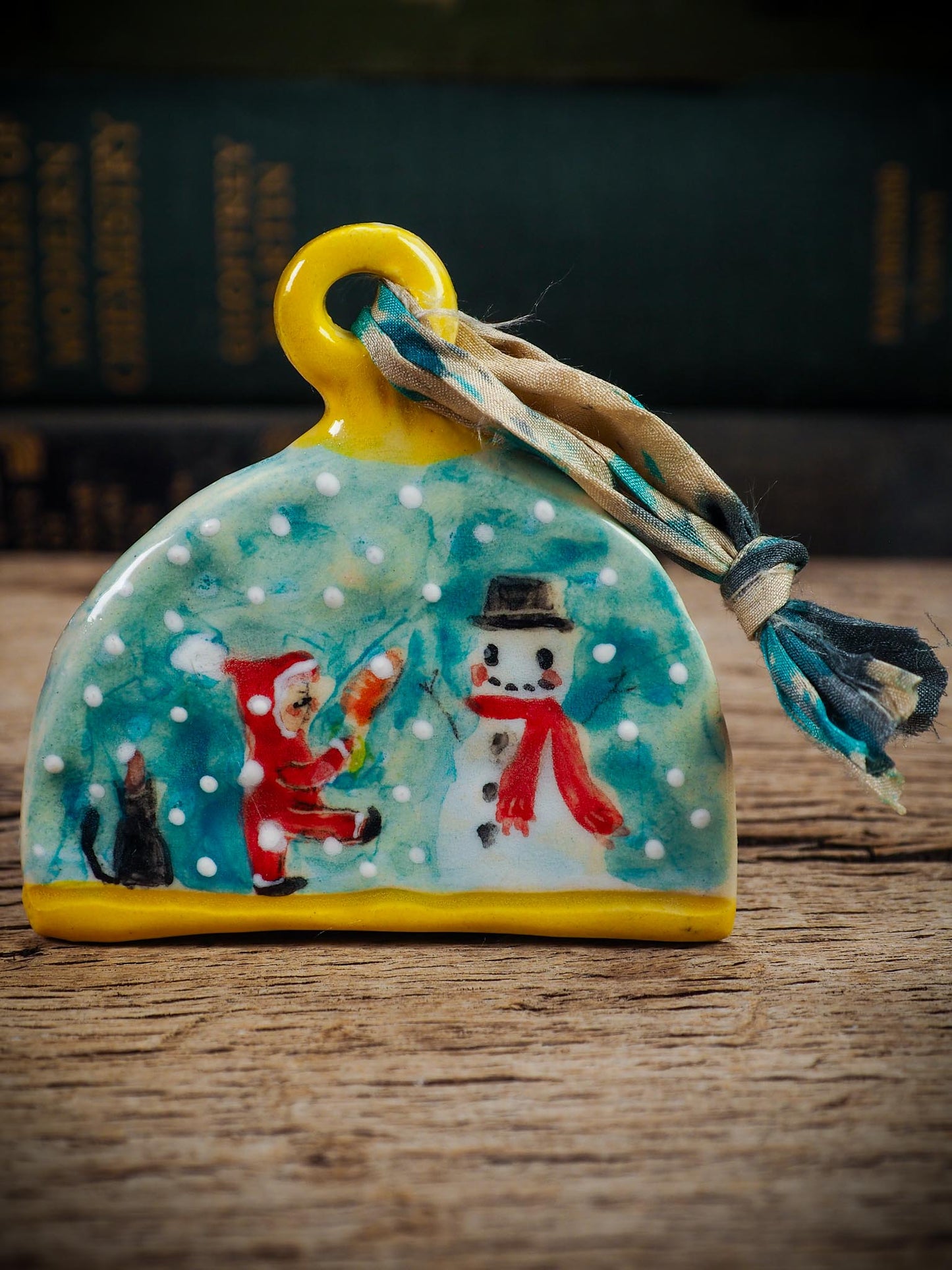 Handmade ceramic ornament with snowman, little Santa, and snowfall, created by Idania Salcido Danita Art for Christmas decorating or gifting.