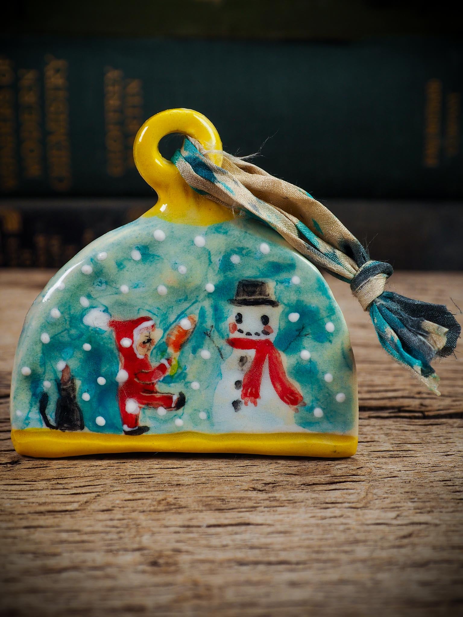 Handmade ceramic ornament with snowman, little Santa, and snowfall, created by Idania Salcido Danita Art for Christmas decorating or gifting.