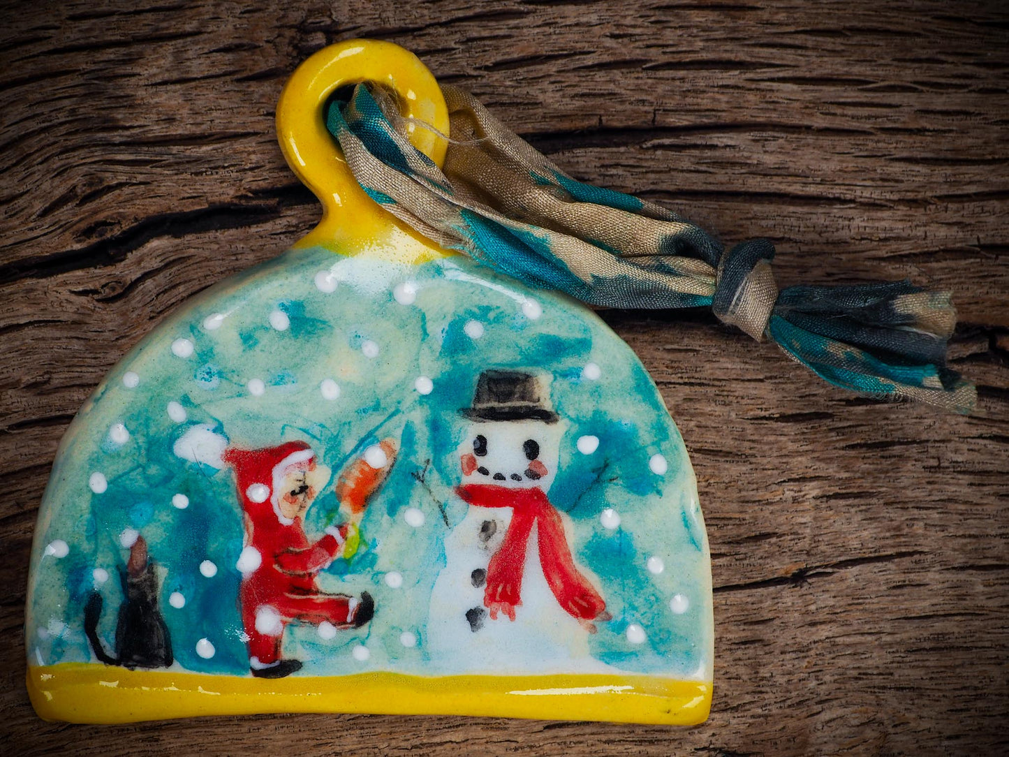 Handmade ceramic ornament with snowman, little Santa, and snowfall, created by Idania Salcido Danita Art for Christmas decorating or gifting.