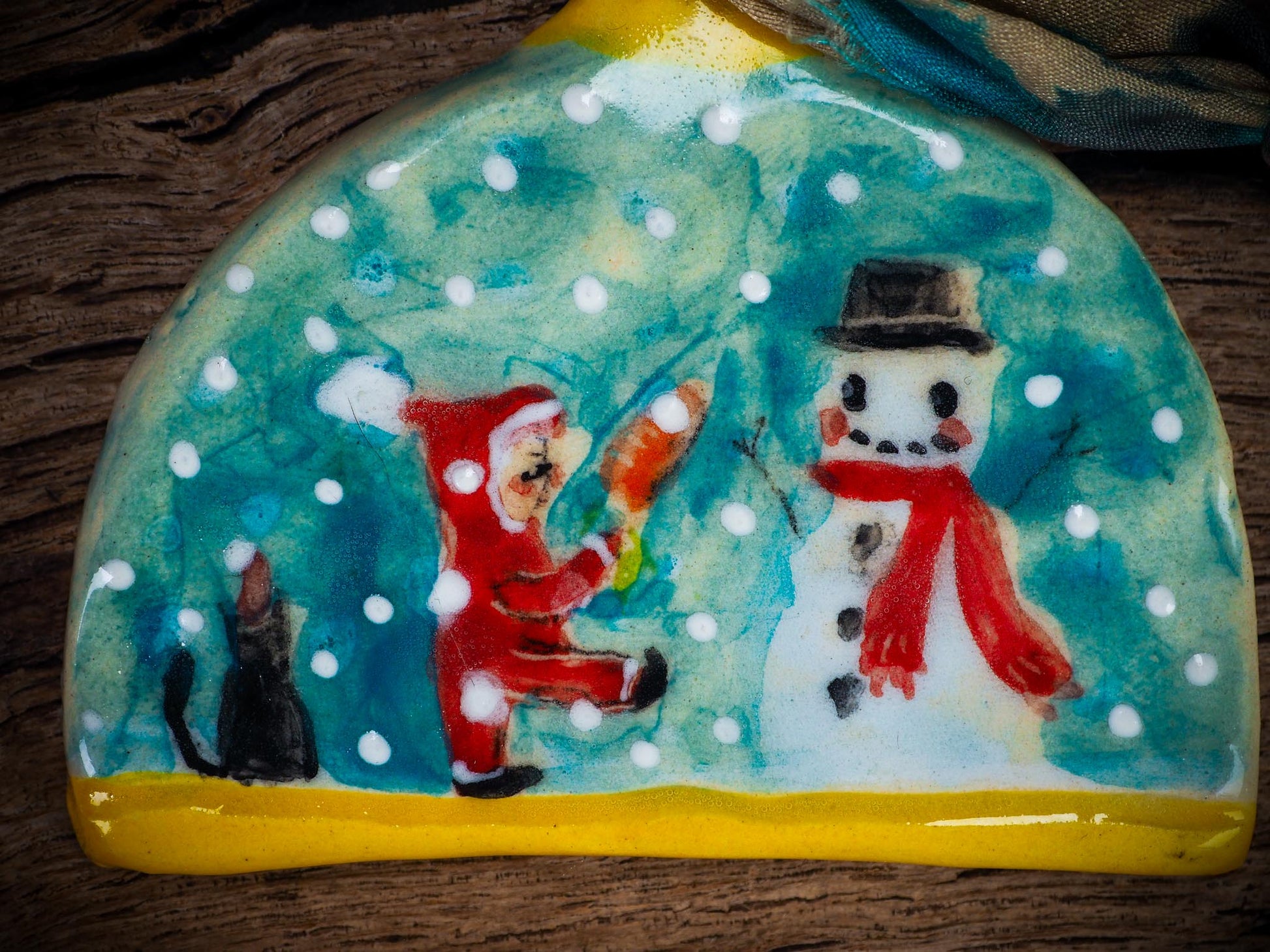 Handmade ceramic ornament with snowman, little Santa, and snowfall, created by Idania Salcido Danita Art for Christmas decorating or gifting.