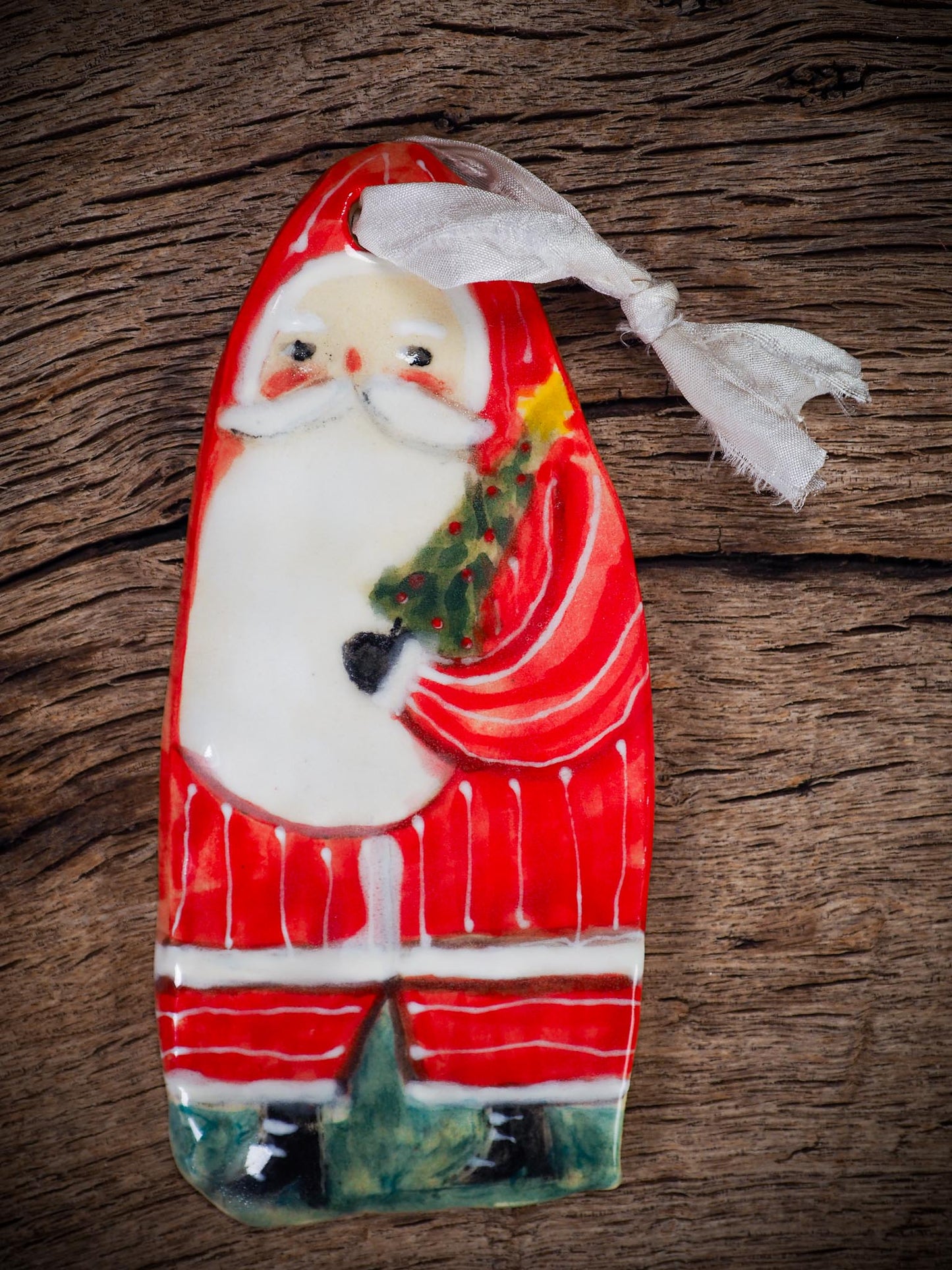 Handmade ceramic Santa figure ornament with red coat and ribbon, created by Idania Salcido Danita Art for Christmas decoration or gifting.