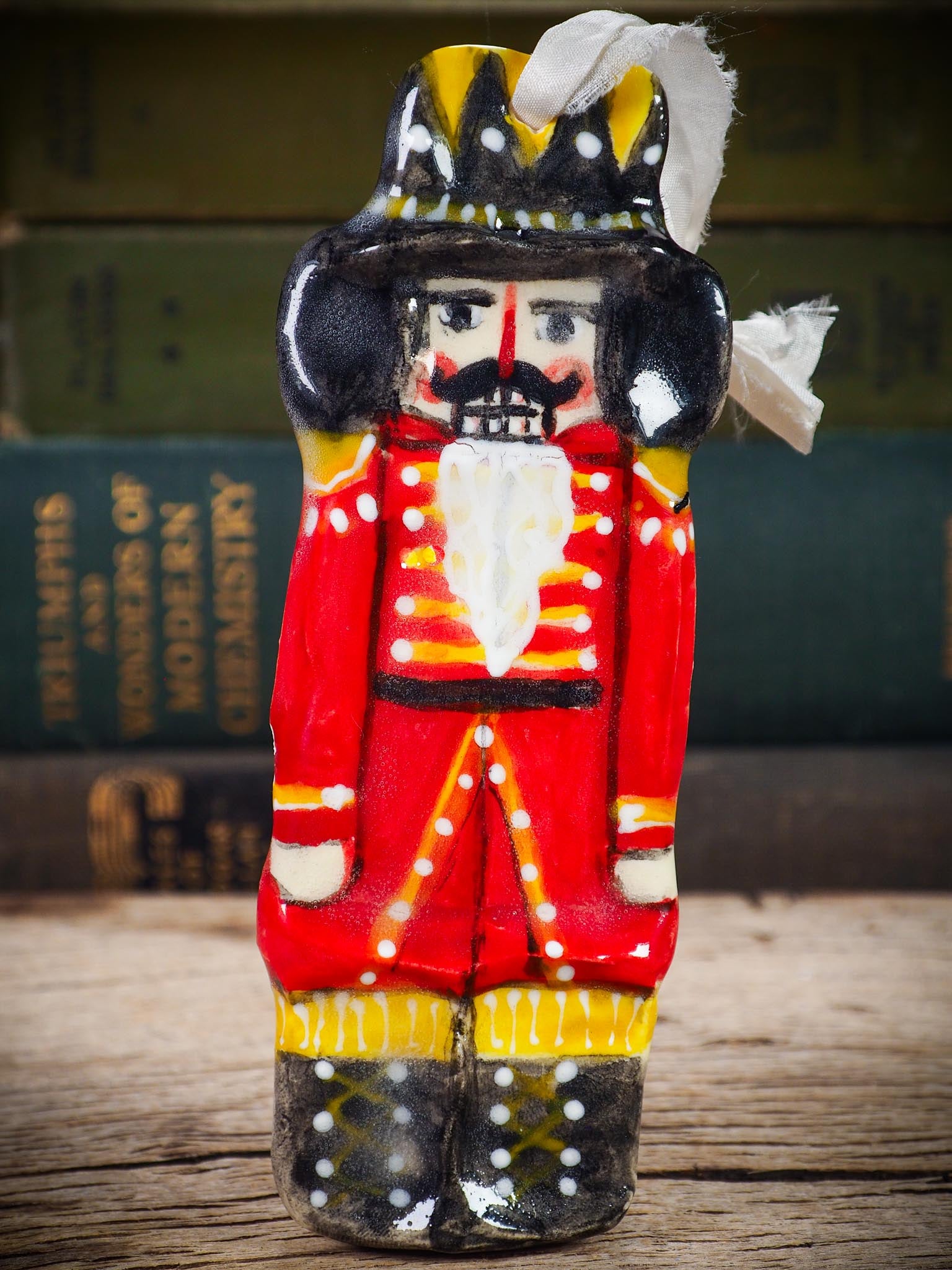 Handmade ceramic nutcracker ornament with red uniform and ribbon, created by Idania Salcido Danita Art for Christmas decoration or gifting.
