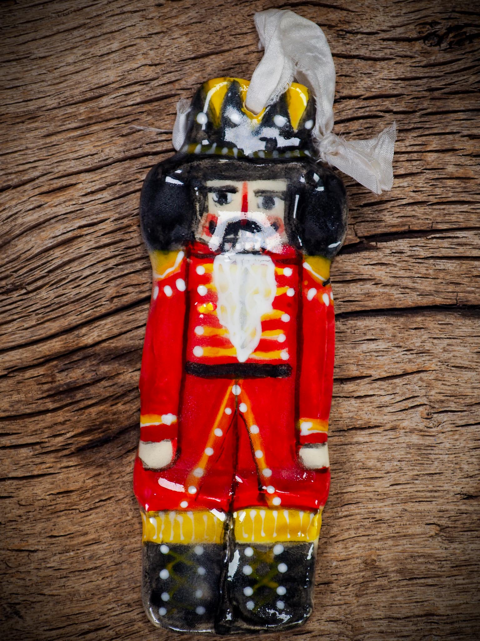 Handmade ceramic nutcracker ornament with red uniform and ribbon, created by Idania Salcido Danita Art for Christmas decoration or gifting.