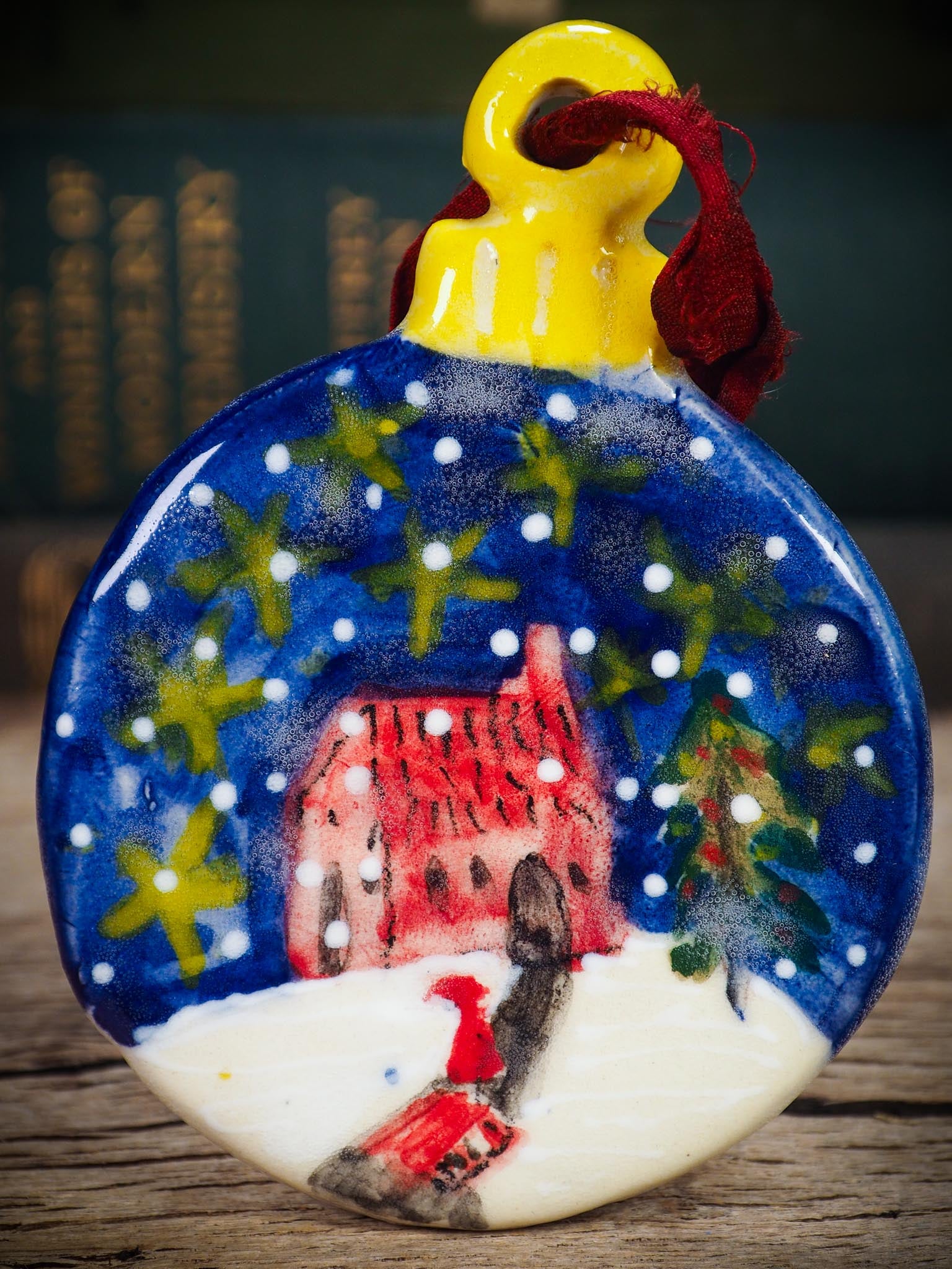 Handmade ceramic winter night ornament with red house, snowy scene, and painted stars, created by Idania Salcido aka Danita Art for Christmas decorating or gifting.